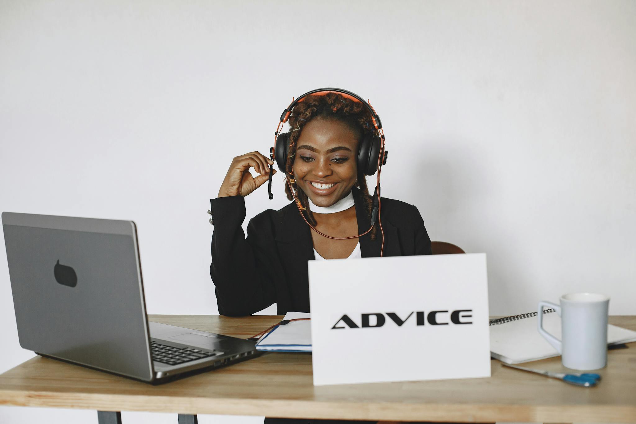 An African American woman smiling while providing online advice using a laptop and headphones.