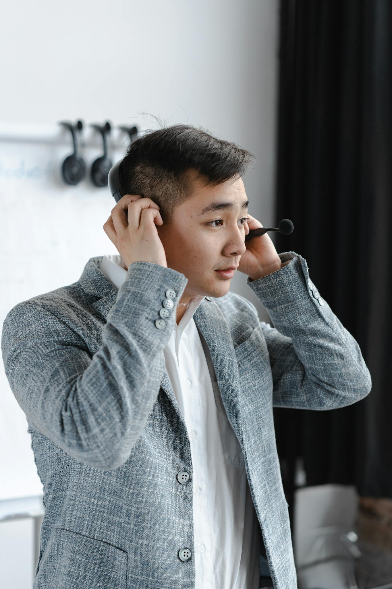 Asian man in a gray suit adjusting his headset for a call. Ideal for customer service or business themes.