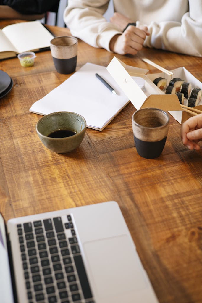 Colleagues having a lunch meeting with sushi and coffee, working at a wooden desk.