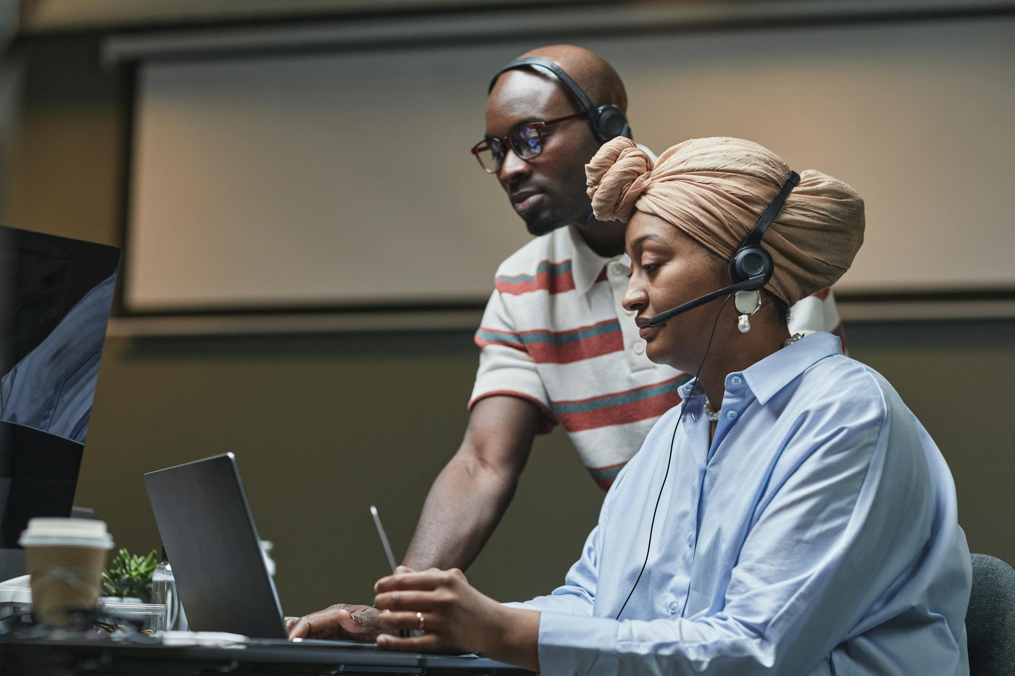 Coworkers collaborating in a modern office with headsets and laptops, focused on multitasking.
